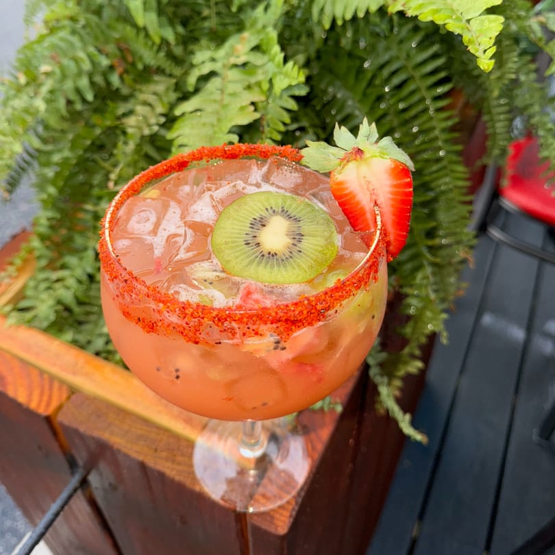 A vibrant El Paso Tacos & Tequila margarita with a chili-lime rim, garnished with kiwi and strawberry.