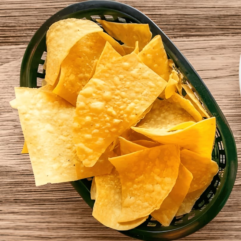 A dark green basket overflowing with golden, crispy tortilla chips on a wooden table.