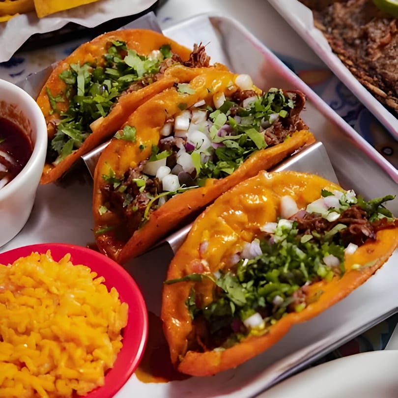 Three birria tacos with cilantro and onions, served with rice and dipping sauce.
