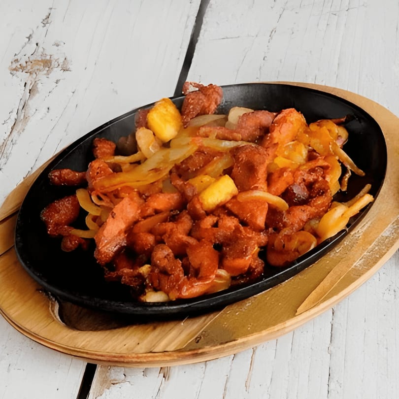 Sizzling Mexican fajitas with chicken, onions, and pineapple served in a black skillet on a wooden board.