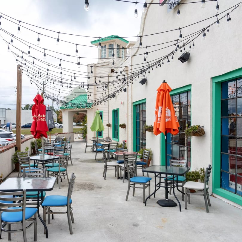 Outdoor patio of El Paso Tacos & Tequila with tables, chairs, umbrellas, and string lights.