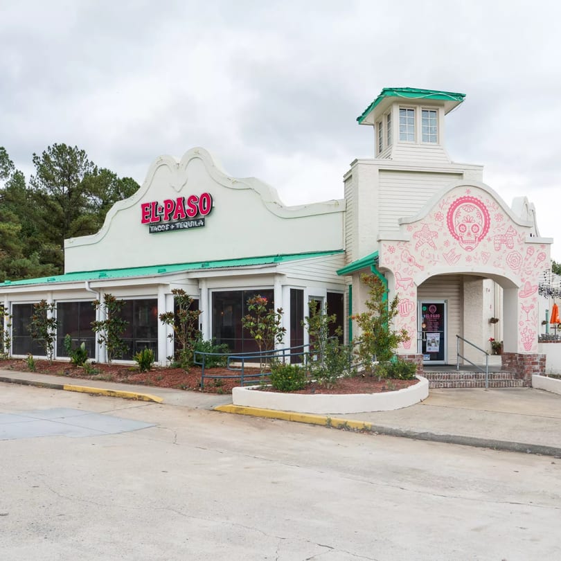 Exterior of El Paso Tacos & Tequila, a white building with a green roof and pink skull mural.