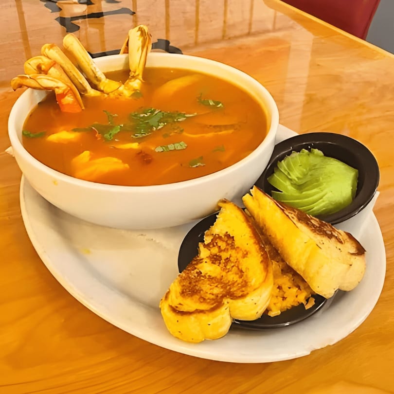 A bowl of El Paso Tacos & Tequila's Mexican seafood soup with crab legs, avocado, and bread.