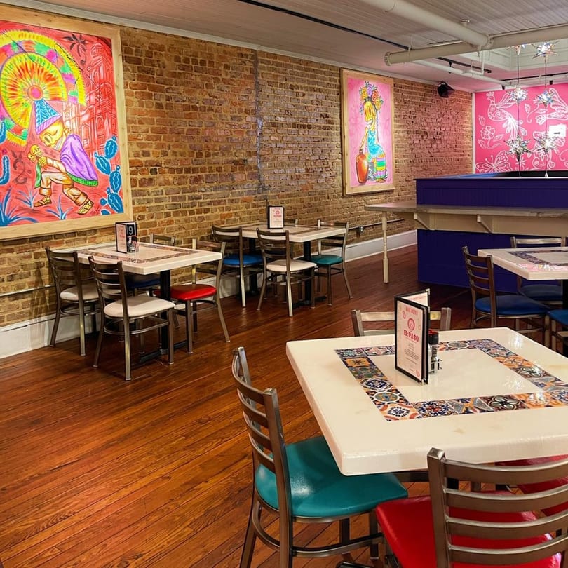 El Paso Tacos & Tequila dining room with brick walls, colorful art, and tables with patterned tile accents.