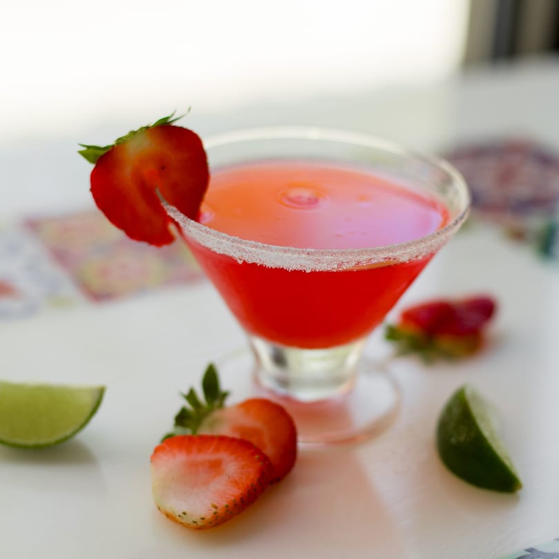 A vibrant strawberry margarita in a salt-rimmed glass, garnished with fresh strawberries and lime.