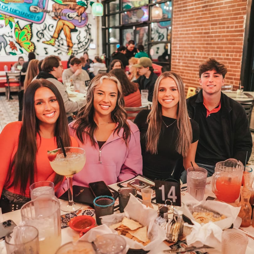 Four smiling young adults at a table with drinks and chips at El Paso Tacos & Tequila.