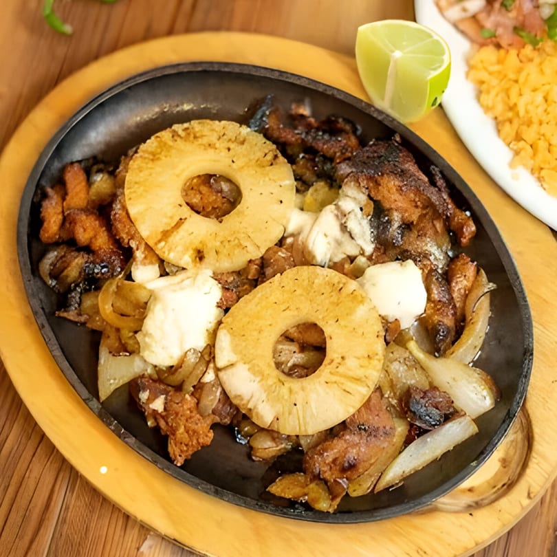 Sizzling Mexican fajitas with grilled pineapple, onions, and chicken, served with a lime wedge.