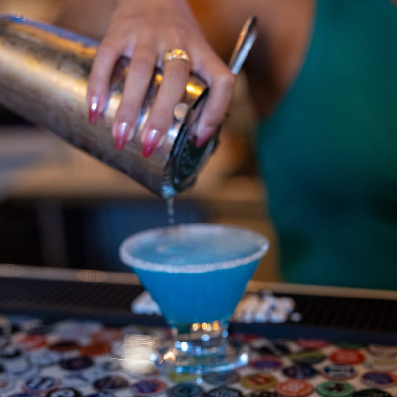 Bartender pouring a vibrant blue margarita with a salted rim into a glass at El Paso Tacos & Tequila.