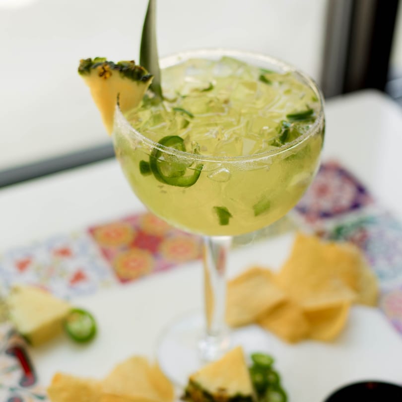 A pineapple and jalapeño margarita with tortilla chips on a colorful patterned surface.