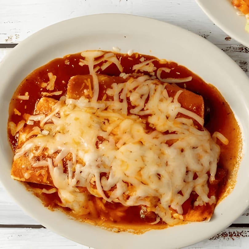 Two cheesy enchiladas covered in red sauce on a white oval plate from El Paso Tacos & Tequila.
