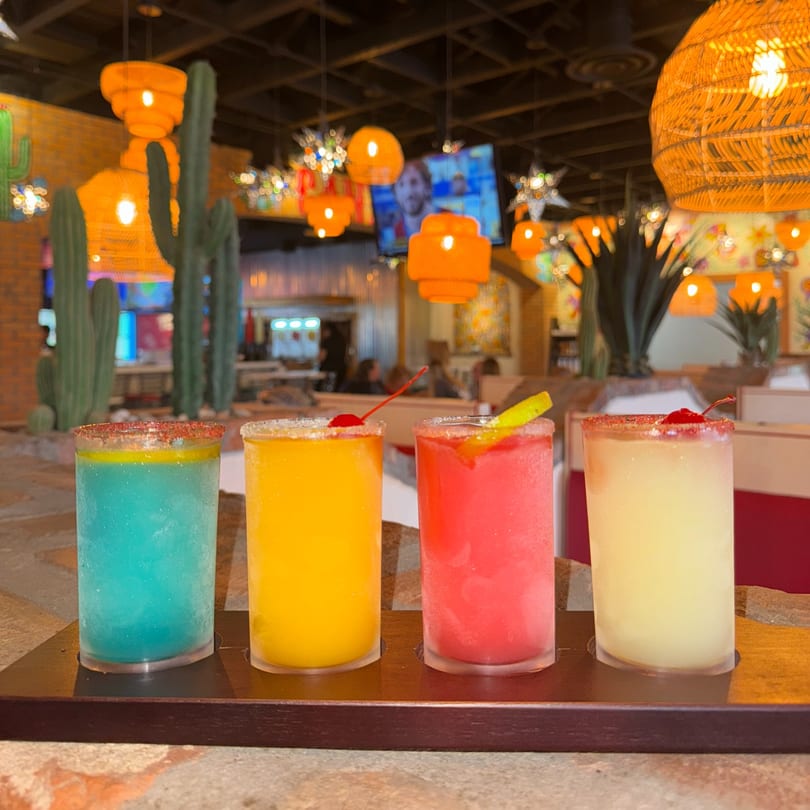 Four colorful frozen margaritas on a tray in a vibrant El Paso Tacos & Tequila restaurant setting.