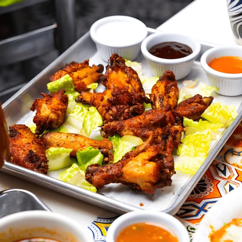 Crispy El Paso Tacos & Tequila chicken wings with lettuce and dipping sauces on a metal tray.