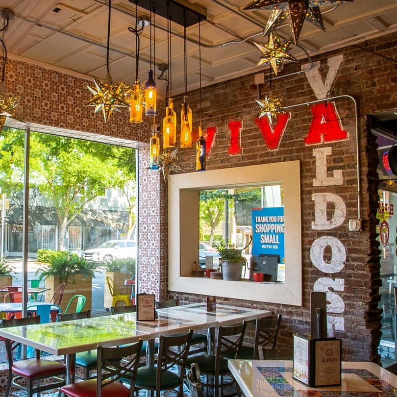 Interior of El Paso Tacos & Tequila with colorful decor, brick walls, and window seating.
