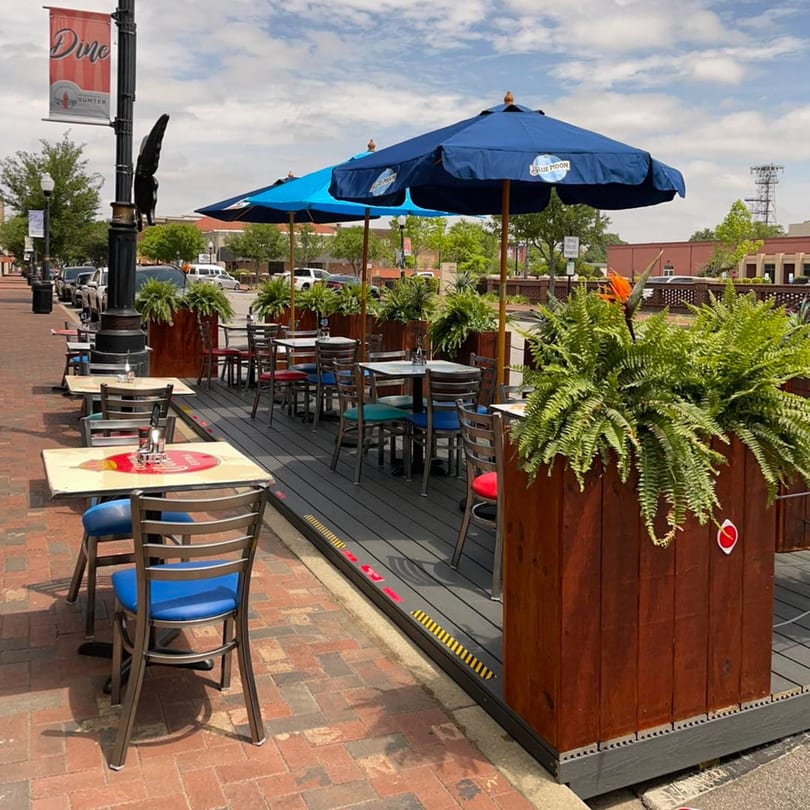 Outdoor patio of El Paso Tacos & Tequila with blue umbrellas, tables, chairs, and plant-filled planters.