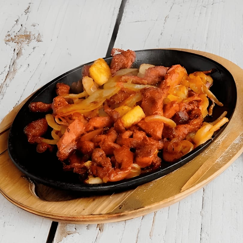 Sizzling fajita meat with onions and peppers in a black skillet on a wooden tray.