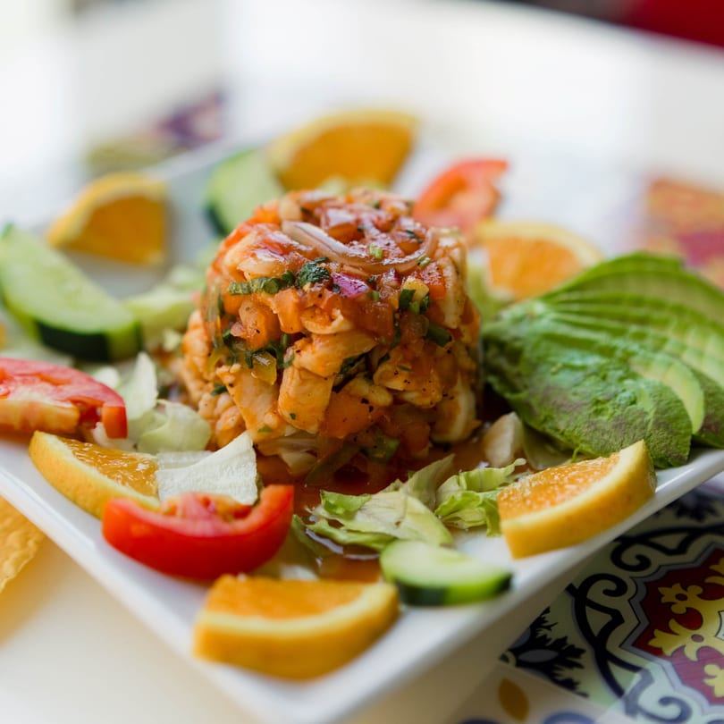 Shrimp ceviche with avocado, orange slices, cucumber, and tomato on a white plate.